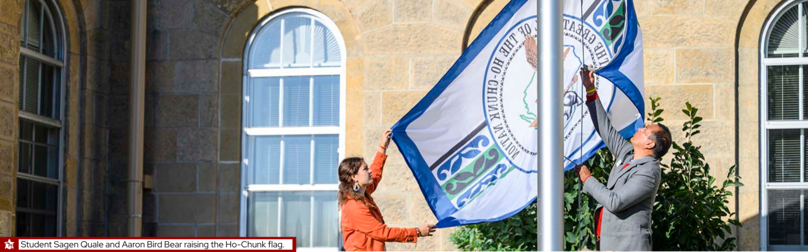 Female student and male faculty raise the Ho-chunk flag at Bascom Hall