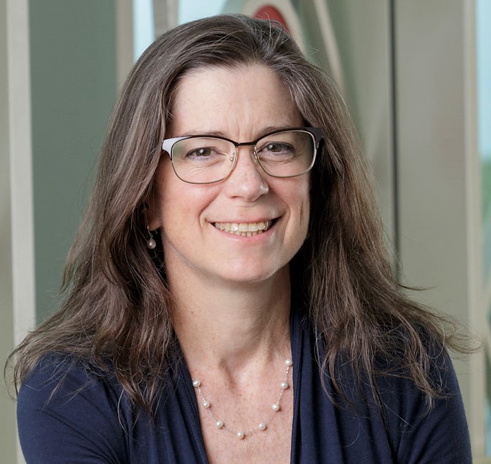 Head shot of woman with brown hair and glasses with neutral background